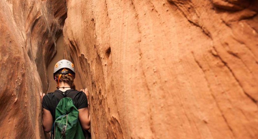 a person wearing a helmet maneuvers through a slot canyon